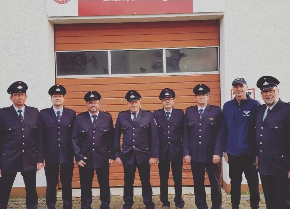Feuerwehrleute und ein Zivilist stehen vor der Feuerwehrstation in Charlottenberg, Rhein-Lahn-Kreis, für ein Gruppenfoto.