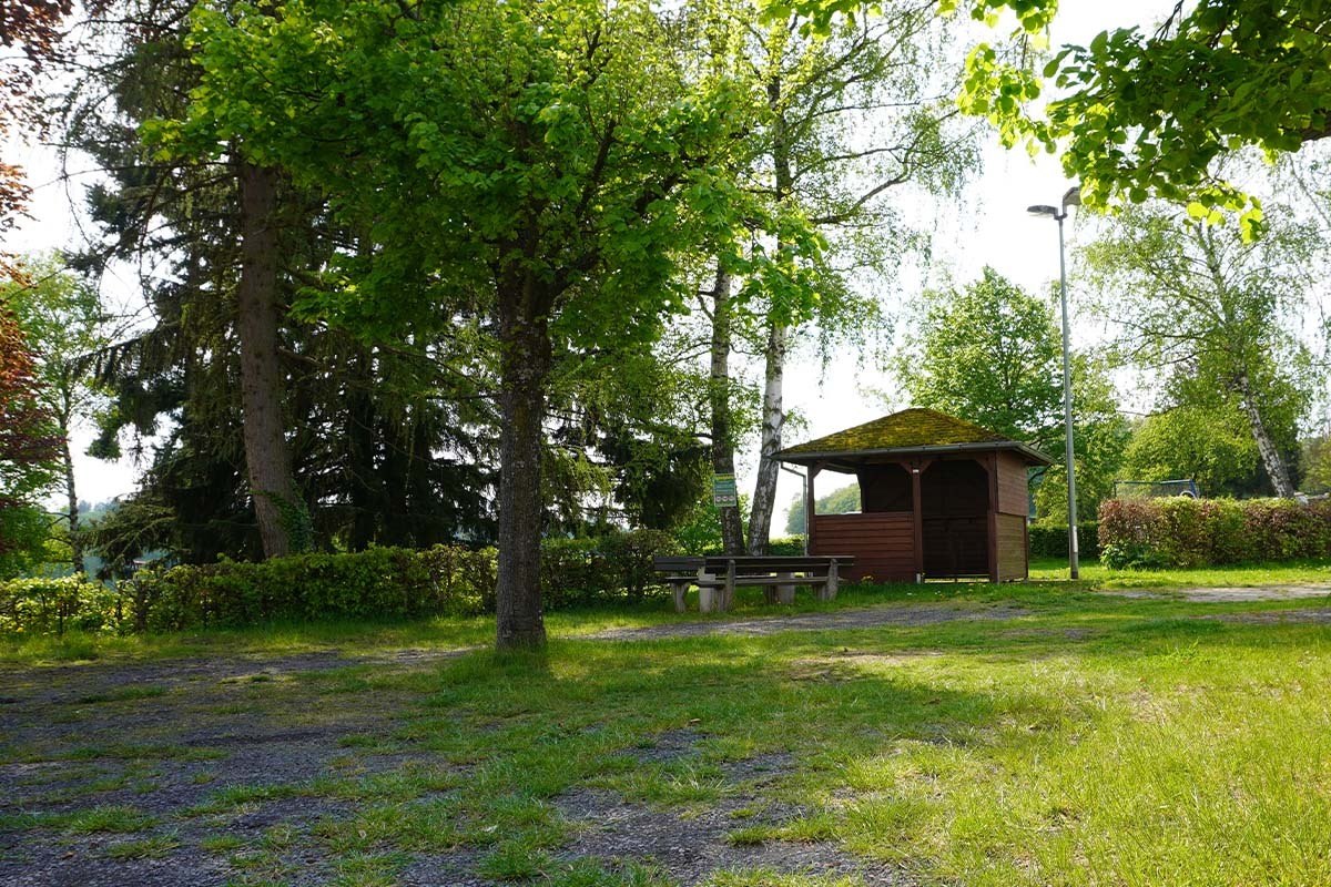 Holzunterstand mit moosbedecktem Dach, Bänken und grünem Wiesengelände – typische Einrichtung in Charlottenberg, naturnaher Ort am Rand des Naturparks Nassau.
