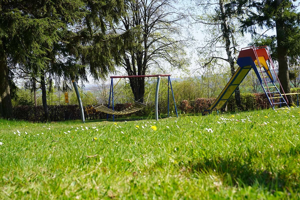 Spielplatz in Charlottenberg mit Schaukel, Rutsche und grünem Rasen, umgeben von Bäumen – ein Beispiel für die naturnahen Freizeitangebote der Gemeinde.