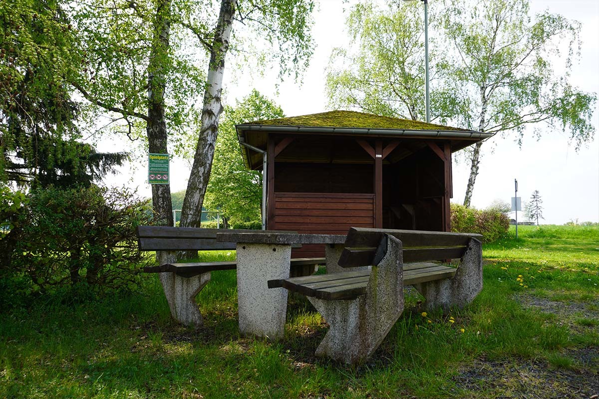 Holzunterstand mit Bänken in einer grünen Umgebung – idealer Rastplatz im naturnahen Charlottenberg am Rand des Naturparks Nassau.